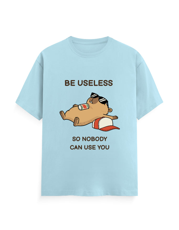 A light blue short-sleeve t-shirt with a cartoon graphic of a sleeping bearded dragon wearing sunglasses and a red-and-white cap. The text reads 'BE USELESS' above the graphic and 'SO NOBODY CAN USE YOU' below.