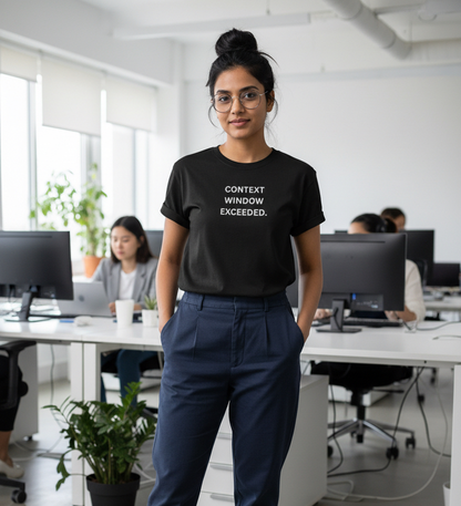 A woman stands in a bright office wearing a black graphic T-shirt with the text 'CONTEXT WINDOW EXCEEDED’