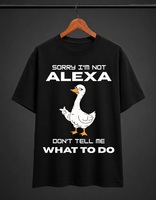 A black short-sleeve t-shirt hanging on a wooden hanger against a dark gray background. The shirt features a white cartoon goose graphic with orange beak and feet, accompanied by the white text 'SORRY I'M NOT ALEXA DON'T TELL ME WHAT TO DO'.