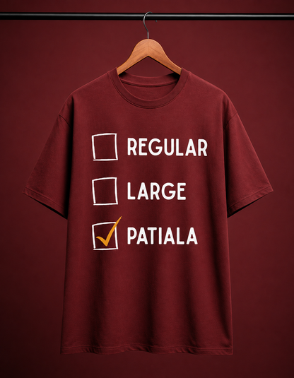 A maroon short-sleeve t-shirt hanging on a wooden hanger against a matching maroon background. The shirt features a white checklist graphic with the words 'REGULAR', 'LARGE', and 'PATIALA', with 'PATIALA' checked in orange.