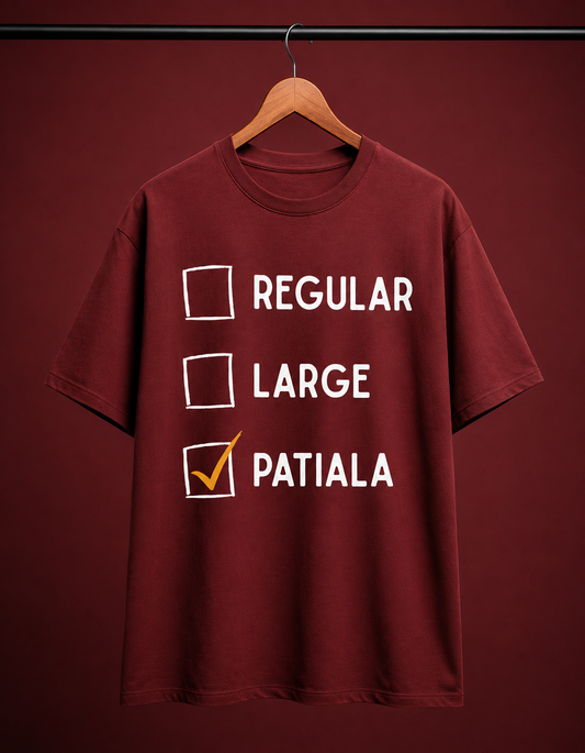 A maroon short-sleeve t-shirt hanging on a wooden hanger against a matching maroon background. The shirt features a white checklist graphic with the words 'REGULAR', 'LARGE', and 'PATIALA', with 'PATIALA' checked in orange.